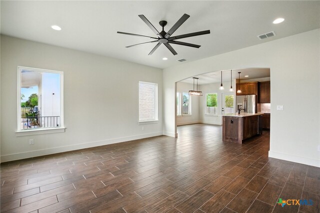 unfurnished living room with visible vents, a ceiling fan, baseboards, and dark wood-style floors