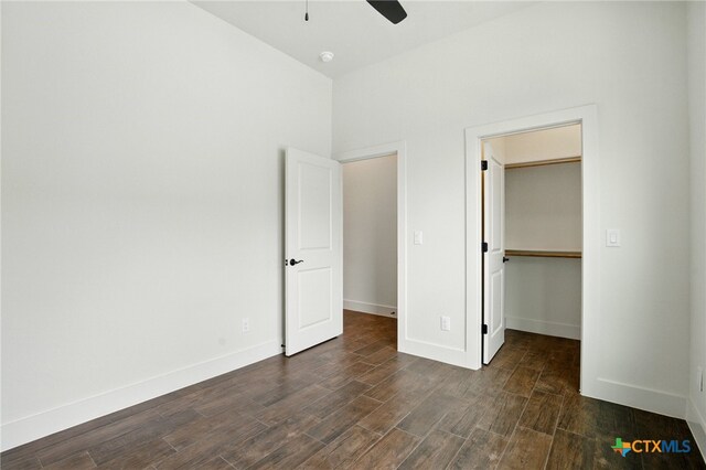 unfurnished bedroom with a ceiling fan, baseboards, a closet, dark wood-style floors, and a spacious closet