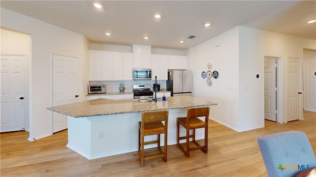 248 Teller Dr, Lockhart, TX 78644 - kitchen with white cabinets, stainless steel appliances, light wood-type flooring, an island with sink, and a breakfast bar area
