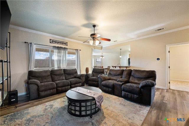 living room featuring hardwood / wood-style flooring, ceiling fan, ornamental molding, and a textured ceiling