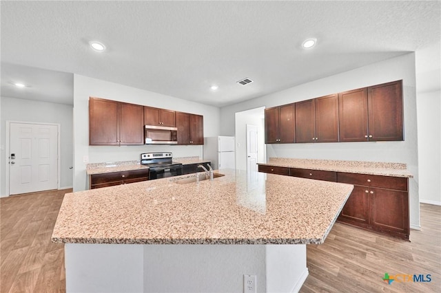 813 Indigo Way, Seguin, TX 78155 - kitchen with stainless steel microwave, a sink, electric range, light wood-style flooring, and an island with sink