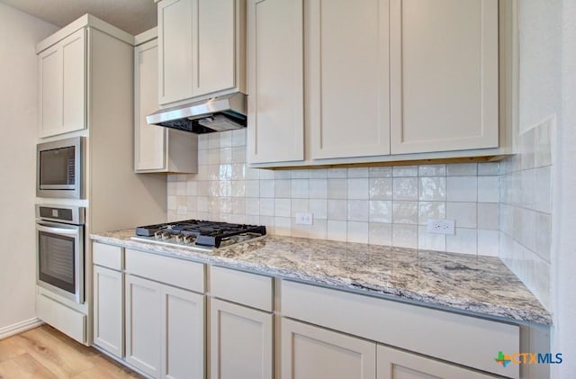 kitchen featuring light stone countertops, white cabinetry, stainless steel appliances, and light wood-type flooring