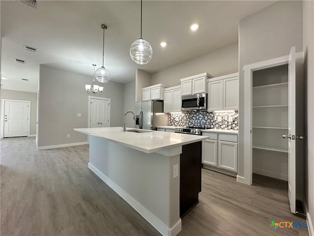 kitchen with sink, appliances with stainless steel finishes, white cabinets, a center island with sink, and decorative light fixtures