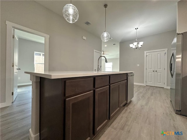 kitchen featuring sink, appliances with stainless steel finishes, a kitchen island with sink, dark brown cabinets, and decorative light fixtures