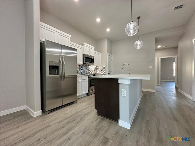 kitchen with appliances with stainless steel finishes, decorative light fixtures, white cabinetry, backsplash, and a center island with sink