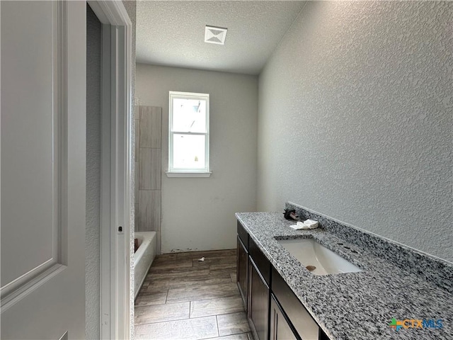 bathroom with vanity, a bathtub, and a textured ceiling