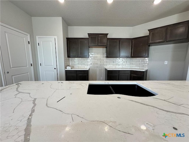 kitchen with light stone counters, dark brown cabinets, decorative backsplash, and a textured ceiling