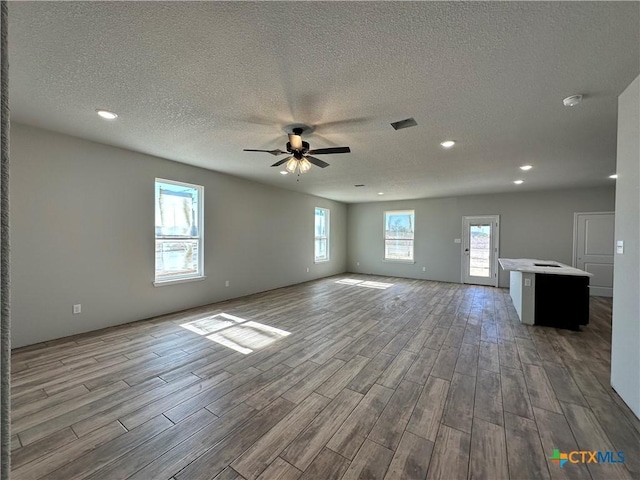 unfurnished living room featuring a textured ceiling, ceiling fan, and light wood-type flooring