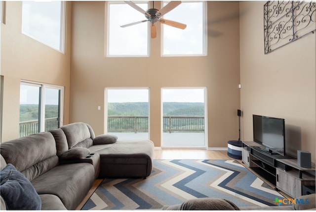 living room featuring a towering ceiling, light hardwood / wood-style flooring, and ceiling fan