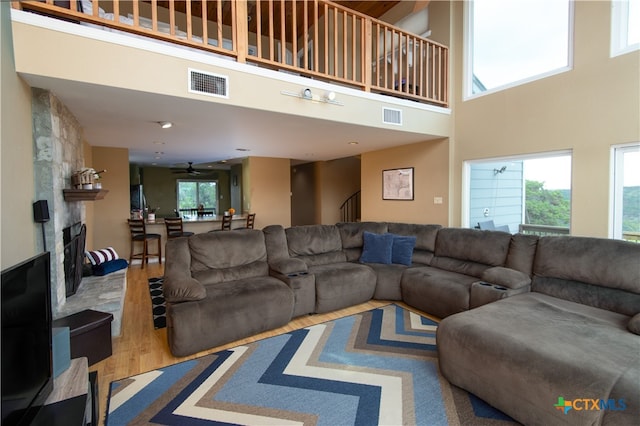 living room featuring a fireplace, a towering ceiling, ceiling fan, and hardwood / wood-style flooring