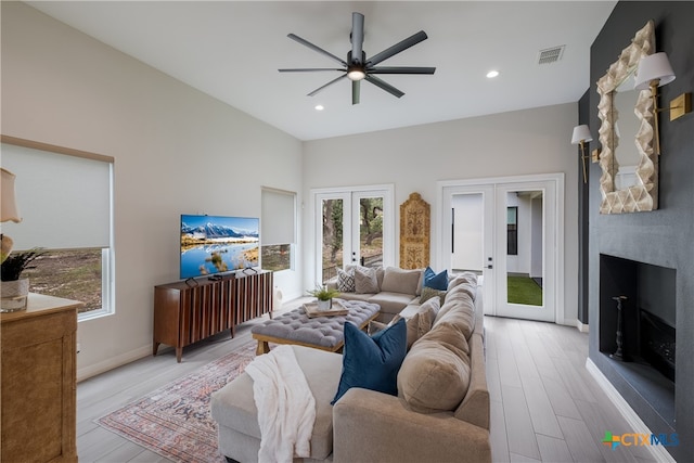 living room with french doors, a fireplace, ceiling fan, and light wood-type flooring