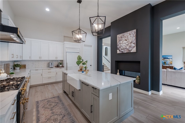 kitchen with white cabinetry, hanging light fixtures, light hardwood / wood-style flooring, a center island, and wall chimney range hood