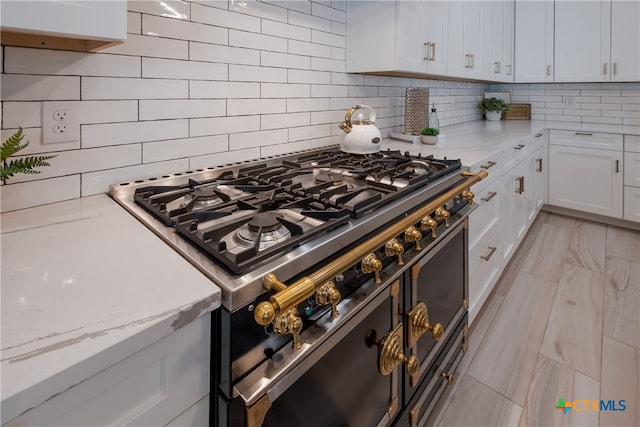 kitchen with stainless steel stove, tasteful backsplash, white cabinets, and light stone counters