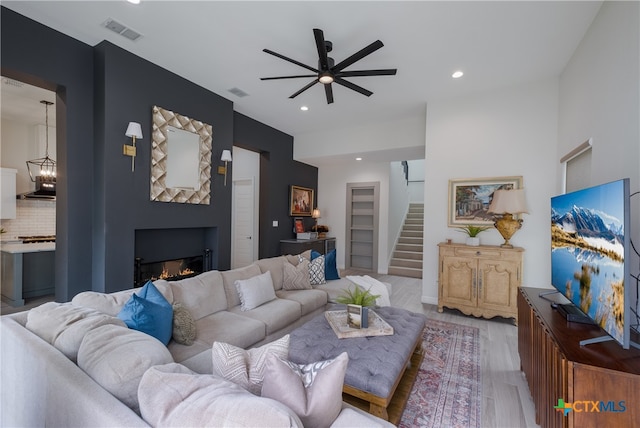 living room featuring ceiling fan with notable chandelier and light hardwood / wood-style flooring