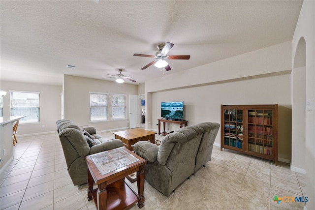 living room featuring light tile patterned floors, visible vents, a ceiling fan, a textured ceiling, and baseboards