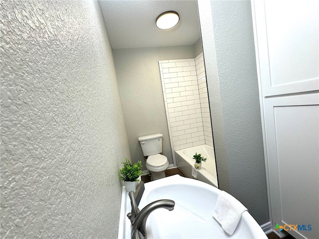 bathroom with toilet, tiled shower / bath, and a textured ceiling