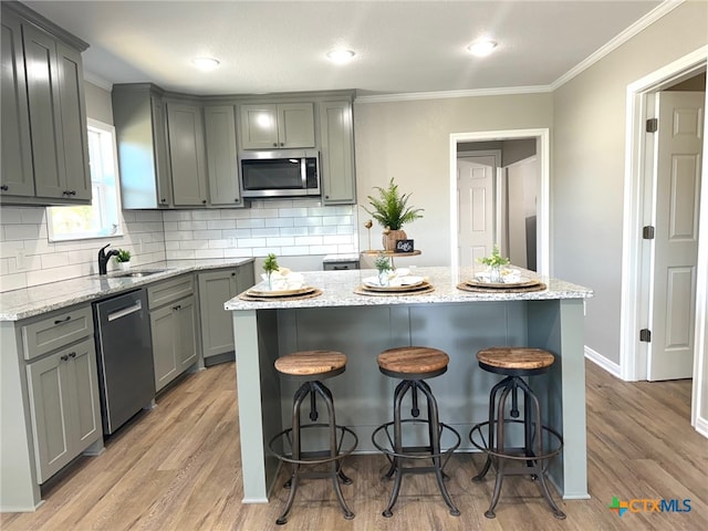 kitchen featuring stainless steel appliances, light hardwood / wood-style floors, sink, crown molding, and a kitchen island