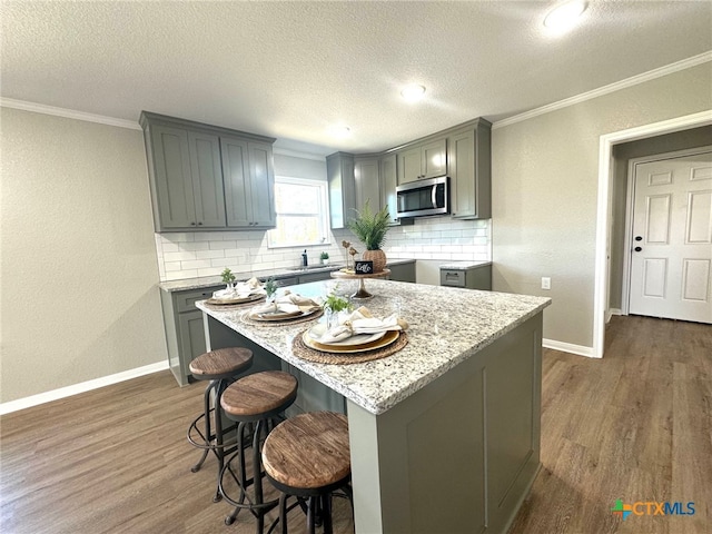 kitchen featuring gray cabinetry, dark hardwood / wood-style flooring, light stone countertops, decorative backsplash, and a center island