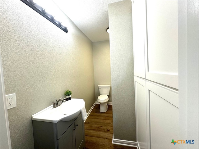 bathroom with wood-type flooring, vanity, toilet, and a textured ceiling