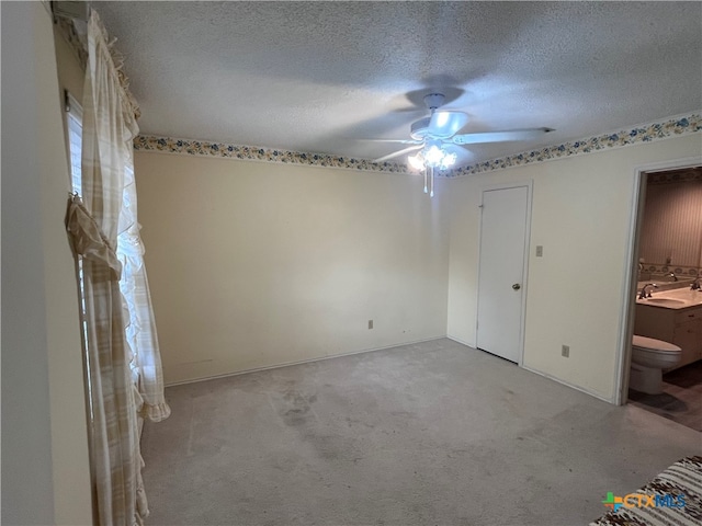 unfurnished bedroom featuring ceiling fan, connected bathroom, a textured ceiling, and light colored carpet