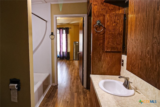 bathroom featuring wood-type flooring, crown molding, vanity, and a bath