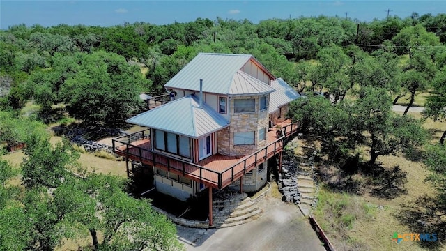 1795 Falconwood Dr, San Marcos, TX 78666 - back of property featuring a wooded view, a deck, a standing seam roof, stone siding, and a metal roof