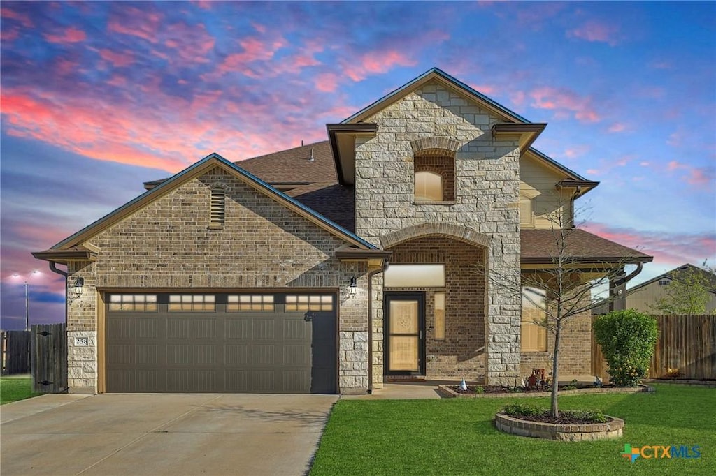 french country inspired facade featuring concrete driveway, stone siding, a front lawn, a garage, and fence