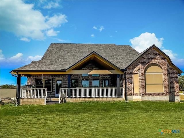 view of front of house featuring brick siding, a porch, a front yard, and roof with shingles