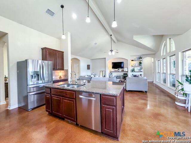 kitchen with an island with sink, a sink, finished concrete flooring, arched walkways, and appliances with stainless steel finishes