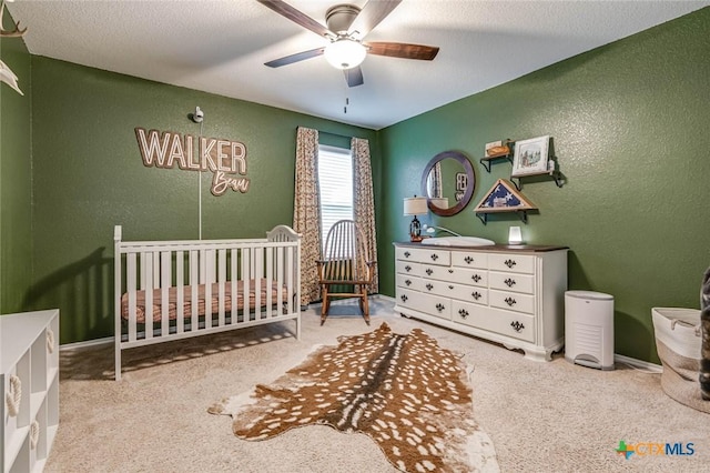 bedroom featuring a textured ceiling, carpet floors, a nursery area, and ceiling fan