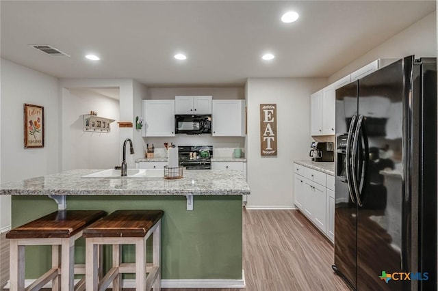 kitchen featuring sink, white cabinetry, a kitchen island with sink, light stone counters, and black appliances