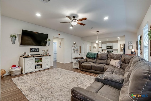 living room with ceiling fan with notable chandelier, vaulted ceiling, and dark hardwood / wood-style floors