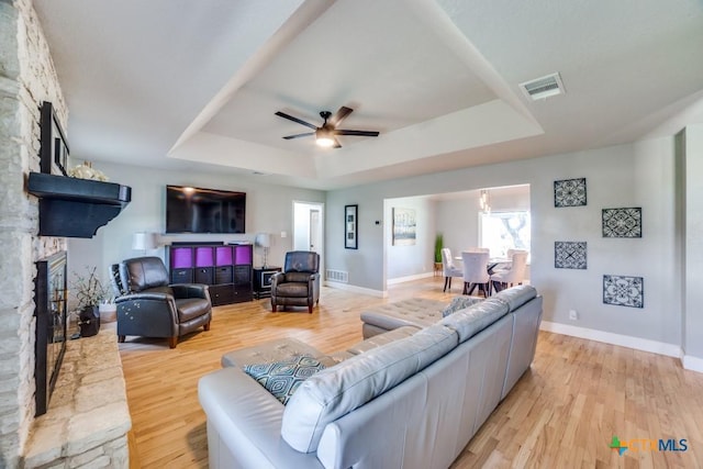 living room featuring a raised ceiling, light wood-style floors, and a fireplace