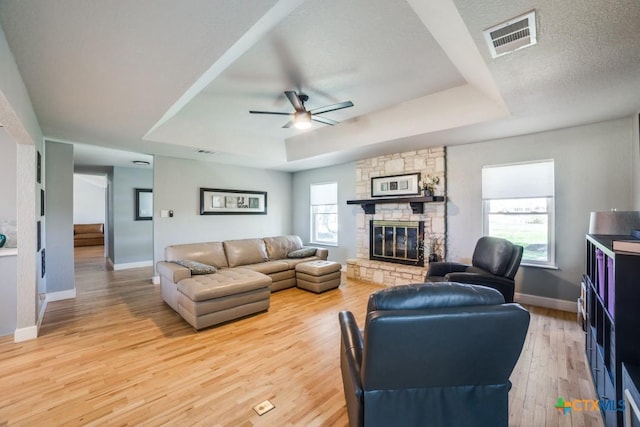 living room featuring visible vents, a raised ceiling, a stone fireplace, and light wood-style flooring