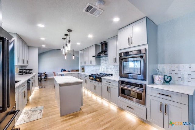 kitchen with visible vents, gas cooktop, a kitchen island, wall chimney exhaust hood, and light wood finished floors