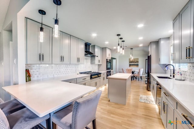 kitchen featuring light countertops, light wood-style floors, gas stovetop, wall chimney exhaust hood, and a sink