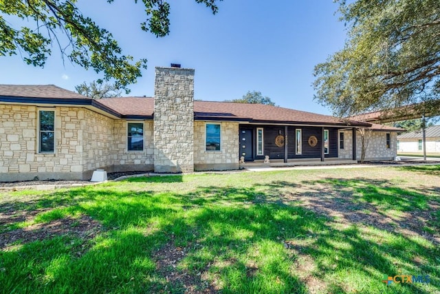 back of property with a yard, stone siding, and a chimney