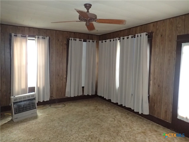 carpeted spare room with plenty of natural light, wood walls, and heating unit