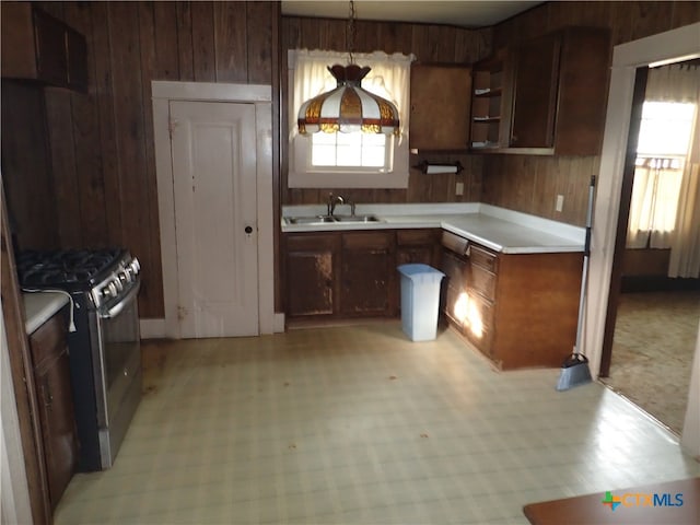 kitchen featuring gas range, pendant lighting, wooden walls, and sink