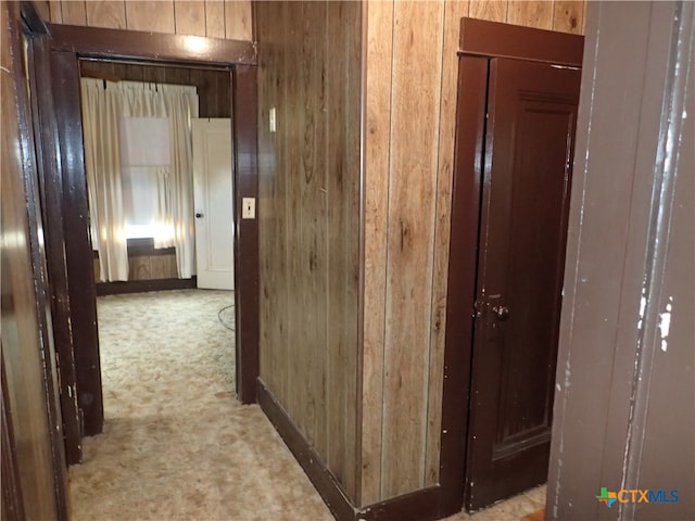 hallway with light colored carpet and wood walls