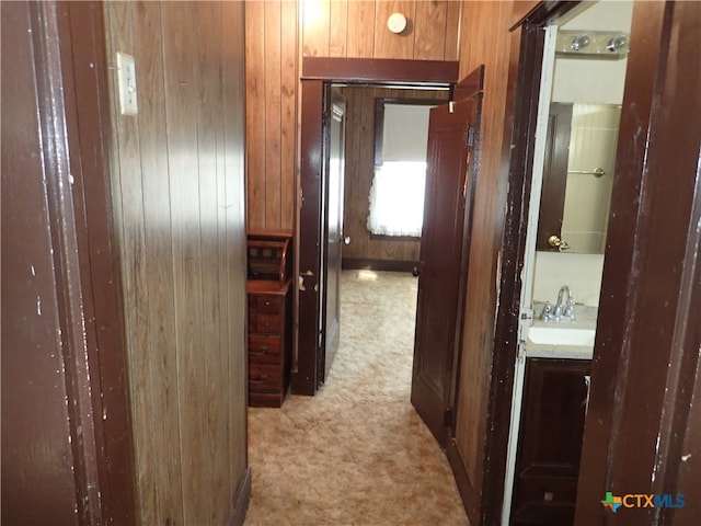 hallway with light colored carpet, sink, and wooden walls