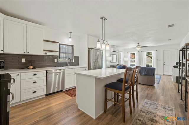 kitchen featuring stainless steel appliances, wood-type flooring, white cabinets, and a kitchen island