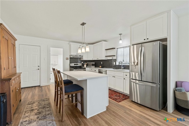 kitchen with a kitchen island, light wood-type flooring, appliances with stainless steel finishes, pendant lighting, and white cabinets