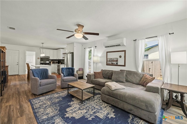 living room featuring a wall unit AC, wood-type flooring, and ceiling fan