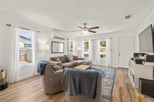 living room featuring light wood-type flooring, ceiling fan, and a wall mounted AC