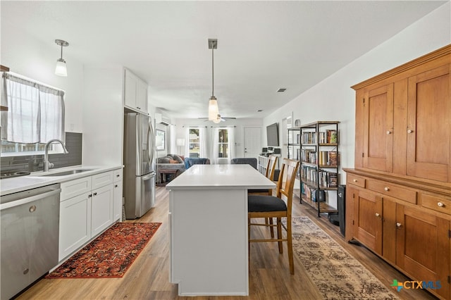 kitchen featuring stainless steel appliances, white cabinetry, sink, light hardwood / wood-style flooring, and a kitchen island