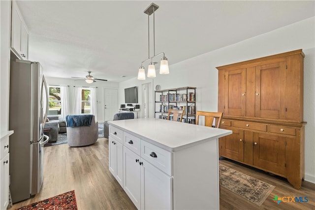 kitchen featuring stainless steel refrigerator, hanging light fixtures, hardwood / wood-style floors, white cabinets, and a center island