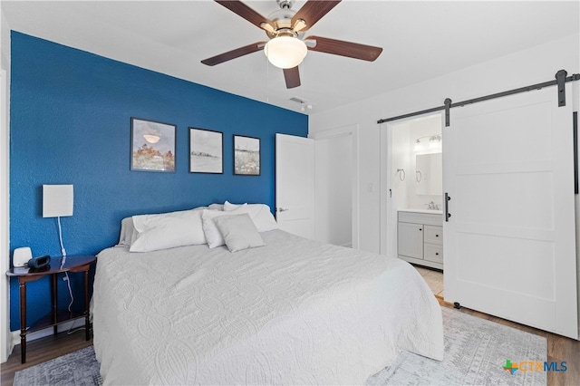 bedroom featuring ensuite bathroom, wood-type flooring, a barn door, and ceiling fan