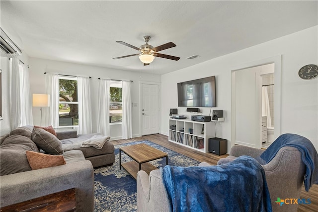 living room with a wall unit AC, wood-type flooring, and ceiling fan