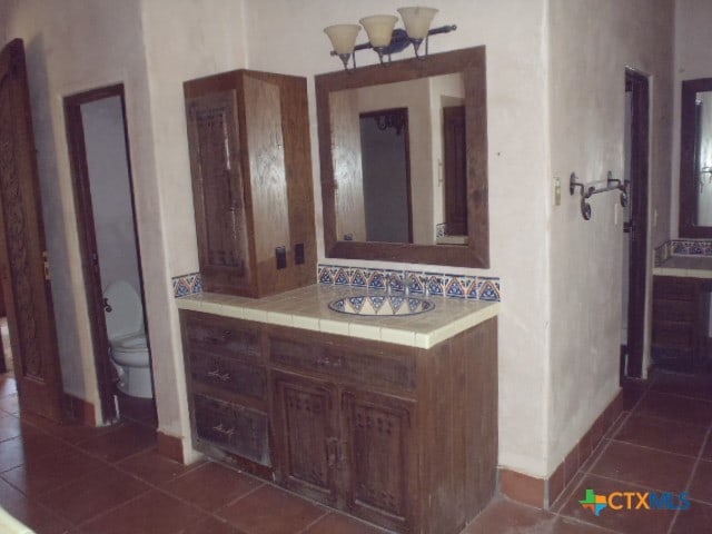 bathroom with toilet, vanity, tile patterned flooring, and a notable chandelier